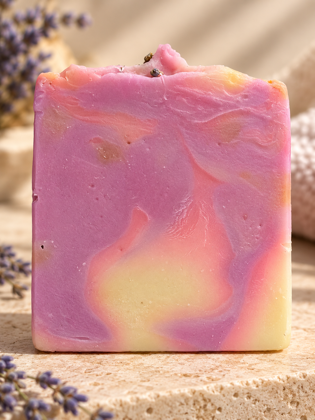 A rectangular handmade soap bar with pink, purple, and pale yellow marbled swirls,