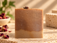 A rectangular handmade soap bar with a two-tone design, featuring a smooth medium brown top half and a lighter tan bottom half,